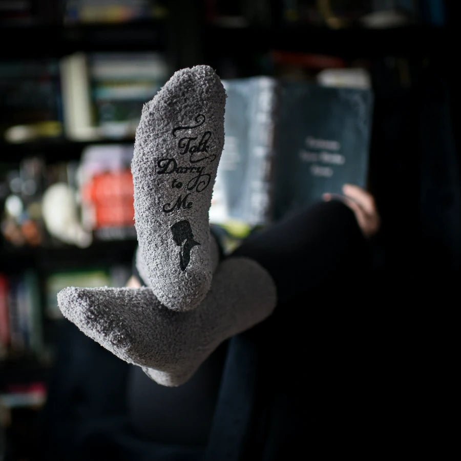 Grey fuzzy socks with &quot;Talk Darcy to Me&quot; in script font with a silhouette of Mr. Darcy.