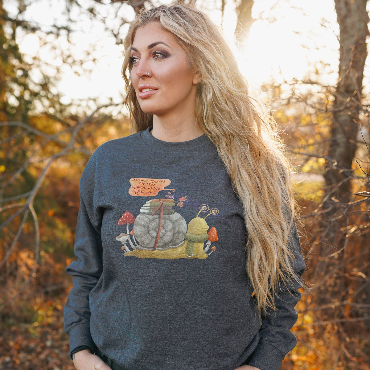 TBR Snail Sweatshirt with books and a teacup strapped to its shell, mushrooms around the snail, and a quote bubble
