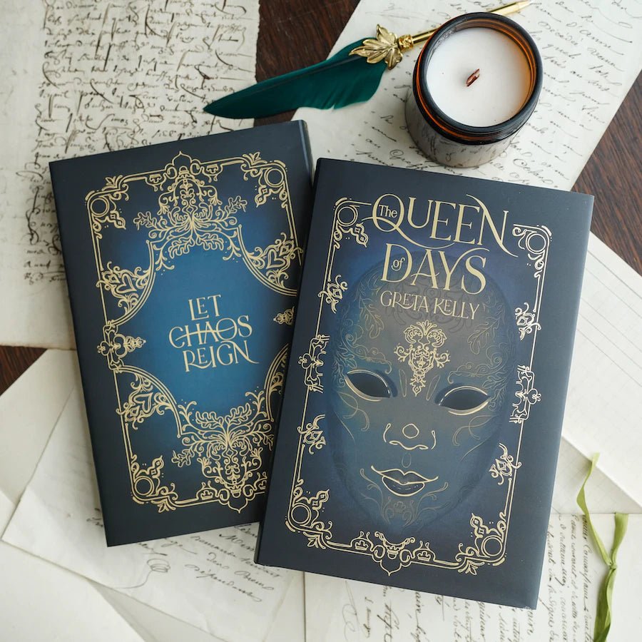 The Queen of Days hardback book with a navy blue cover with gold foiling scrollwork, a gold mask, and designed page edges.