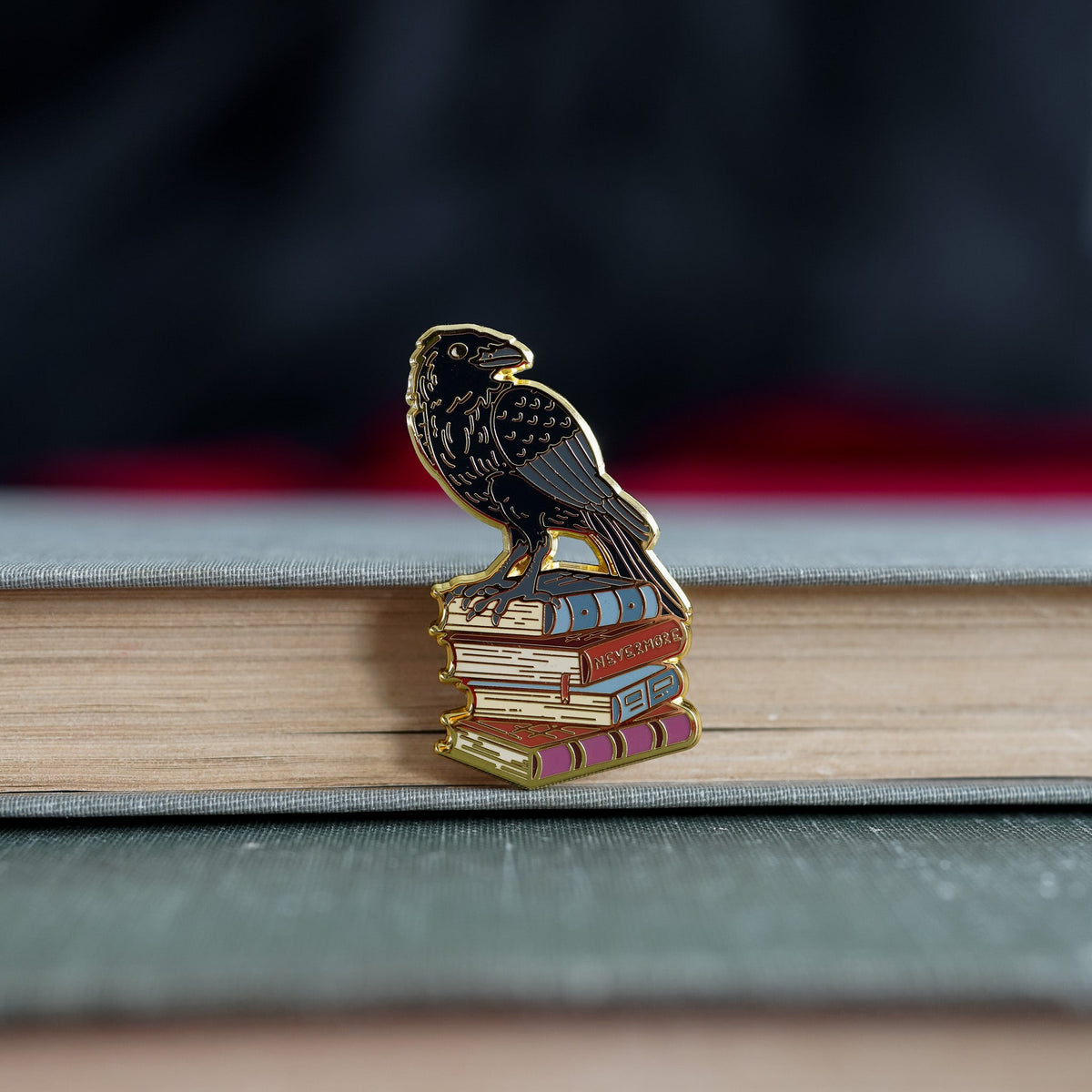 The Raven Critter Collection Enamel Pin with a raven standing on top of four books.