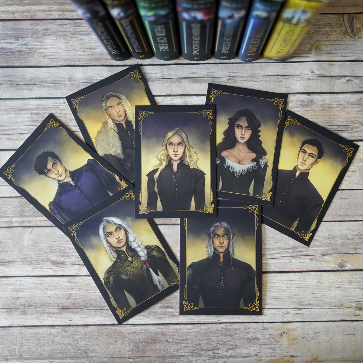 Throne of Glass Art Print set of 7 cards featuring black and gold borders and depicting images of Celaena, Rowan, Dorian, Aedion, Chaol, Manon, and Lysandra