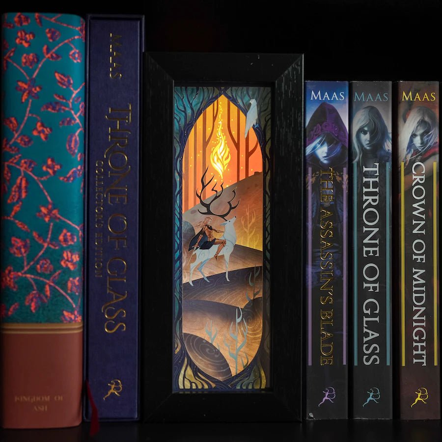 Purple, blue, and yellow Throne of Glass Bookshelf Alley is a black-framed shadowbox with a white papercut design of a woman on a stag.